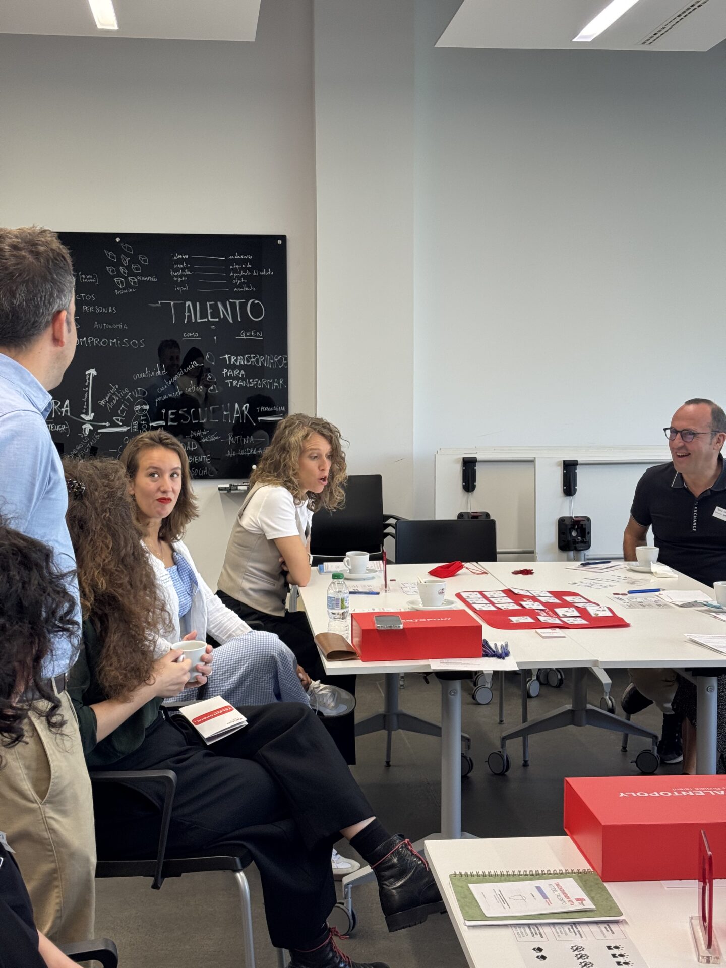 Personas alrededor de una mesa y de pie jugando a un juego creado "Talentopoly".